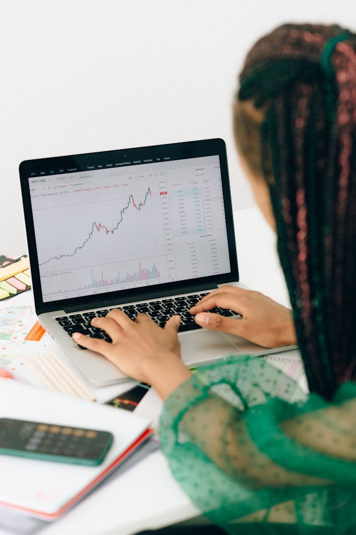 digital A woman working on financial analysis using a laptop with a stock market graph on screen.