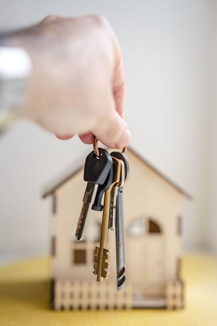 creative Close-up of a hand holding keys with a miniature wooden house in the background, symbolizing real estate investment.